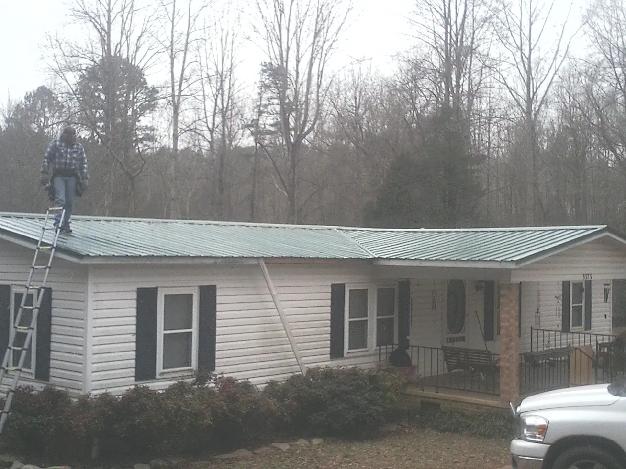 Worker on a ladder beside a new green metal roof on a ranch home in Grandview