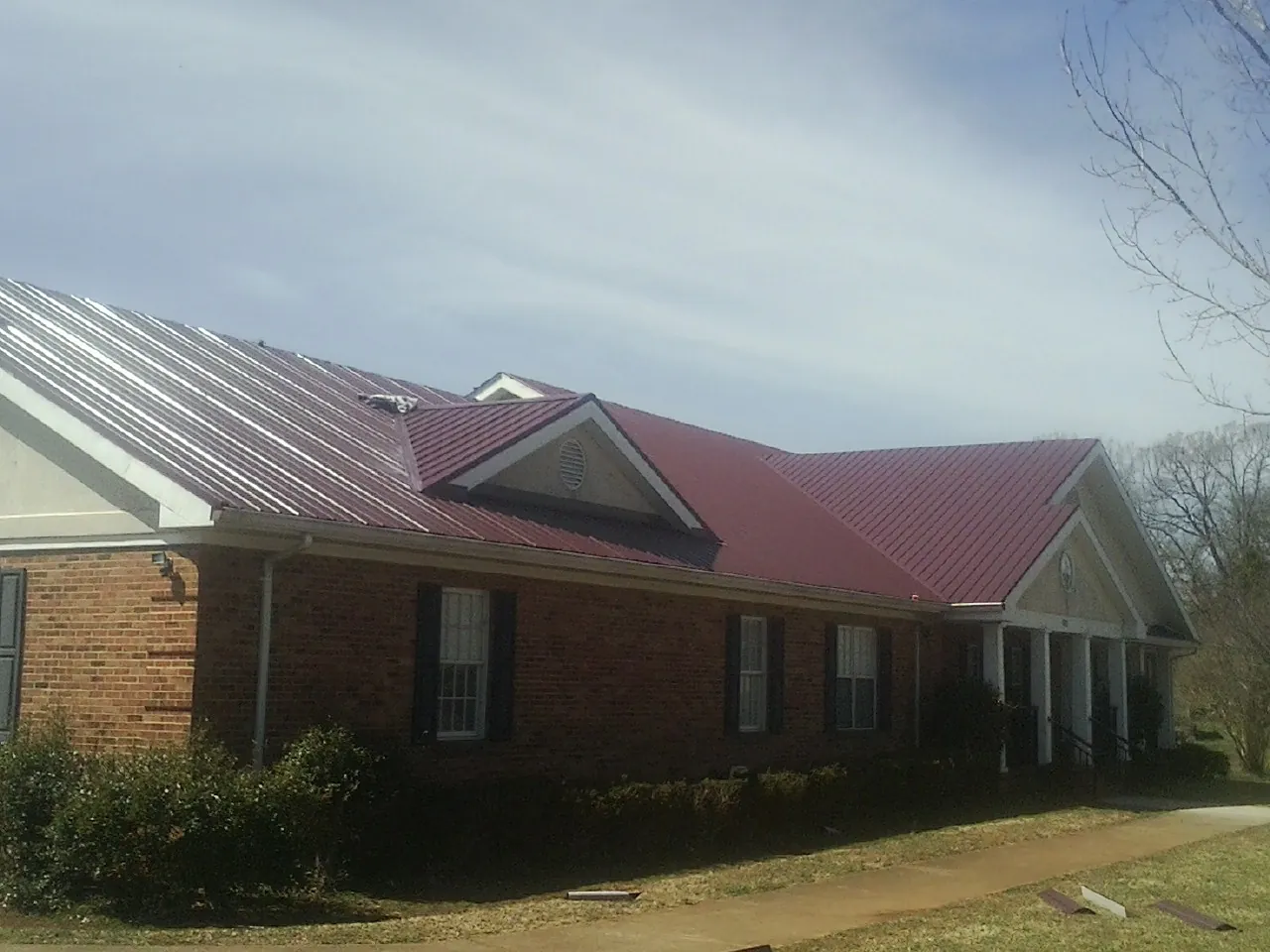 Red metal roof with gabled entries on a long brick building, from a Hail Damage Roof Repair job in Grandview