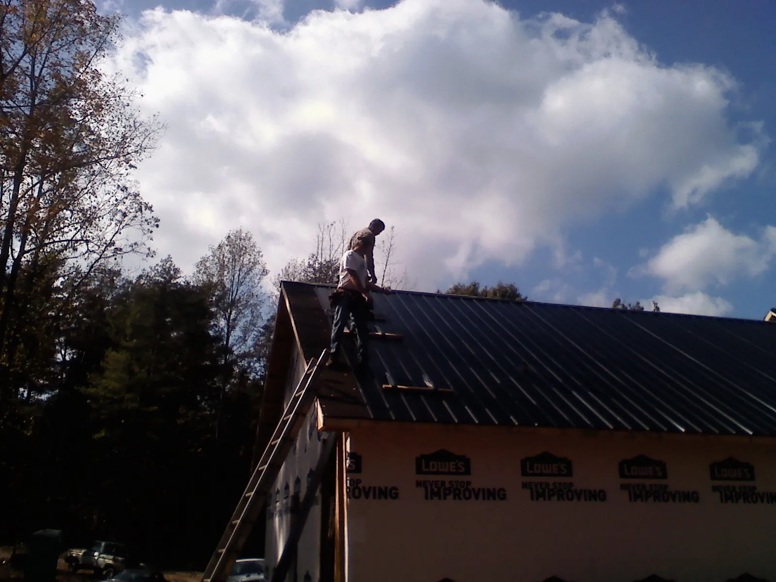 Roofer fastening dark metal panels high against a cloudy sky, from a Roof Inspection job in Grandview